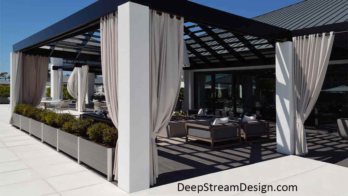 Modern Planters in slate grey no-maintenance recycled plastic lumber and anodized aluminum control access to a modern clubhouse outdoor lounge with long white curtains pulled back around a ceiling shade grid open to the bright blue sky.