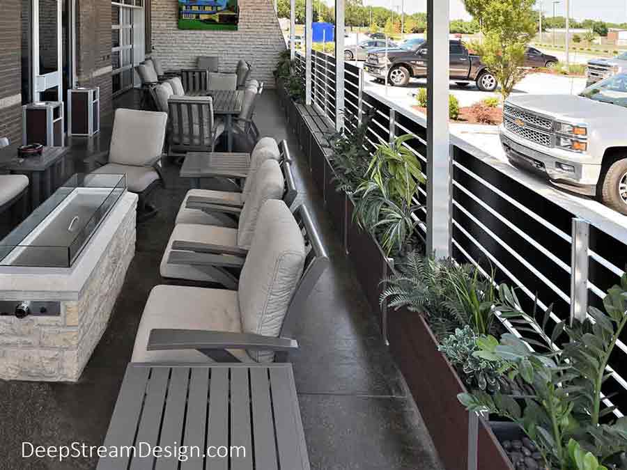 A detailed interior view of an outdoor restaurant smoking section, complete with cushioned chairs, fire pits and DeepStream’s modern Ash-Trash receptacles with ashtray tops, attached to an upscale brick restaurant. Created in an L shape the Ipe Brown 6-foot-high screen wall, with a gate, provided controlled access and is anchored by landscaped Mariner commercial wood planters holding the aluminum planks screen wall panels.